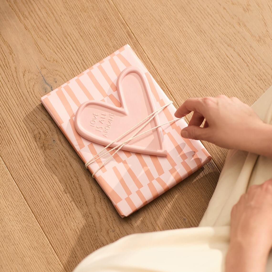 Rosa Herz Teller 'Love is all around' auf verpacktem Geschenk, ideal für liebevolle Anlässe von räder design.